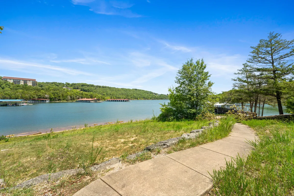 A scenic view of a serene lake bordered by lush greenery and featuring a winding path leading toward the water. This tranquil setting invites outdoor activities such as hiking, walking, and exploring with a pet, and highlights the natural beauty of the Ozarks.