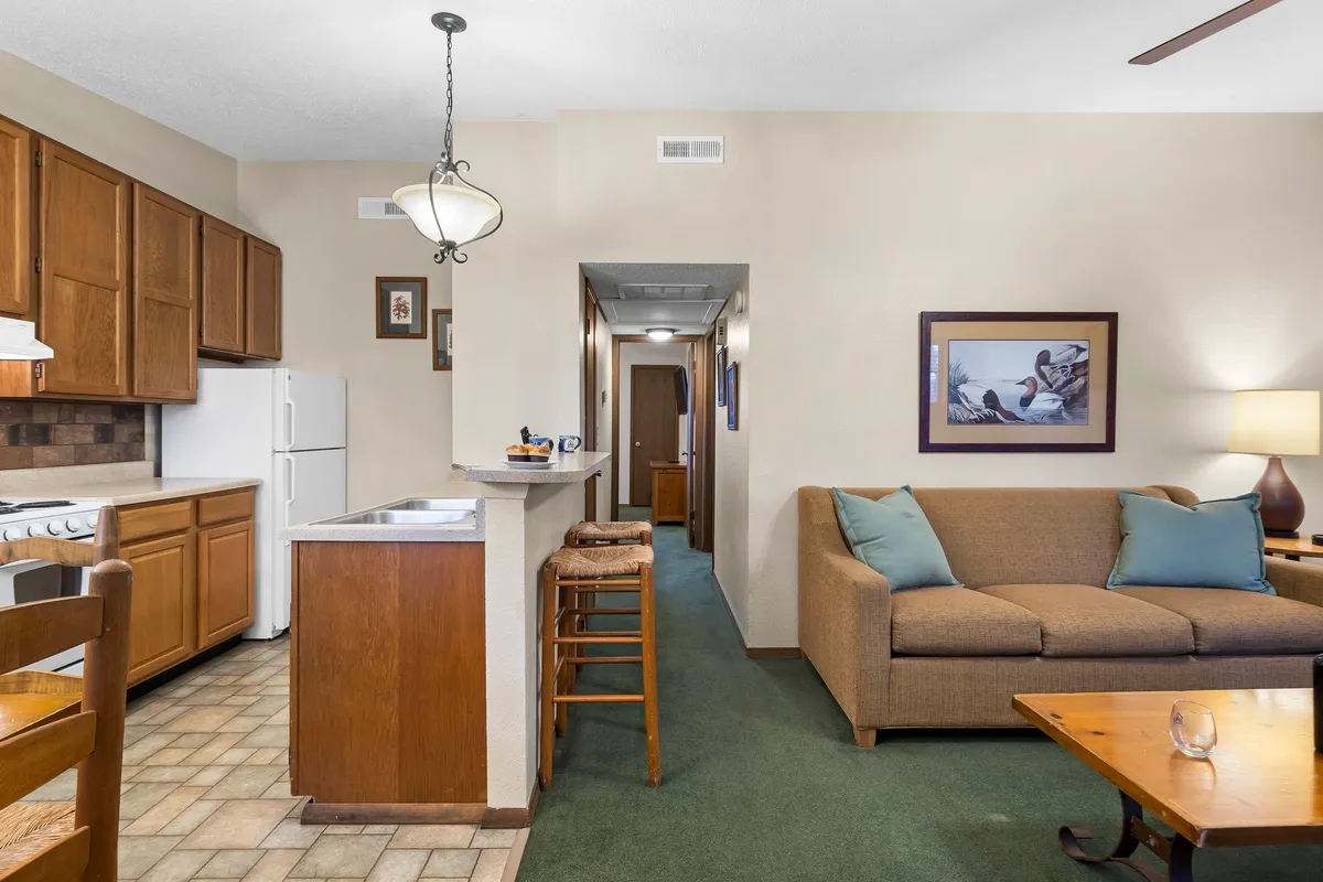 This image features a welcoming, open-plan living space. The kitchen island is visible with seating for guests, seamlessly connecting to the dining area and a cozy sofa. Subtle art decorates the walls, enhancing the homey atmosphere. The scene evokes a sense of togetherness and comfort, highlighting both cooking and dining as social activities.