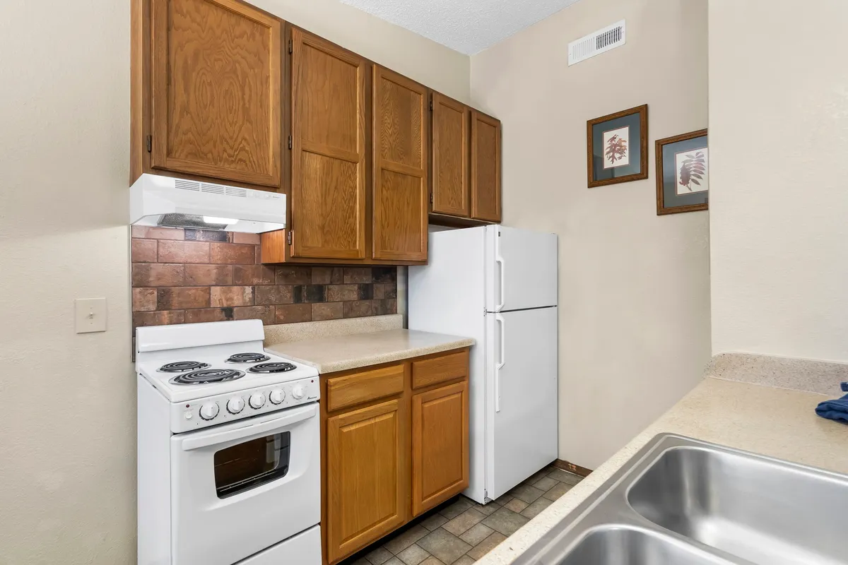 A close-up view of a well-appointed kitchen featuring a stove, refrigerator, polished cabinets, and ample countertop space. The arrangement suggests a fully equipped and functional space, ideal for both casual cooking and more elaborate meal preparation. The cozy lighting enhances the sense of warmth and practicality.
