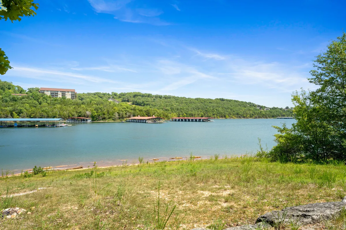 A tranquil scene showing calm lake waters, a distant tree line, and several boathouses extending over the water. The peaceful ambiance suggests ideal moments for fishing, picnicking, or simply watching the sunset, emphasizing the retreat's connection to nature through all seasons.