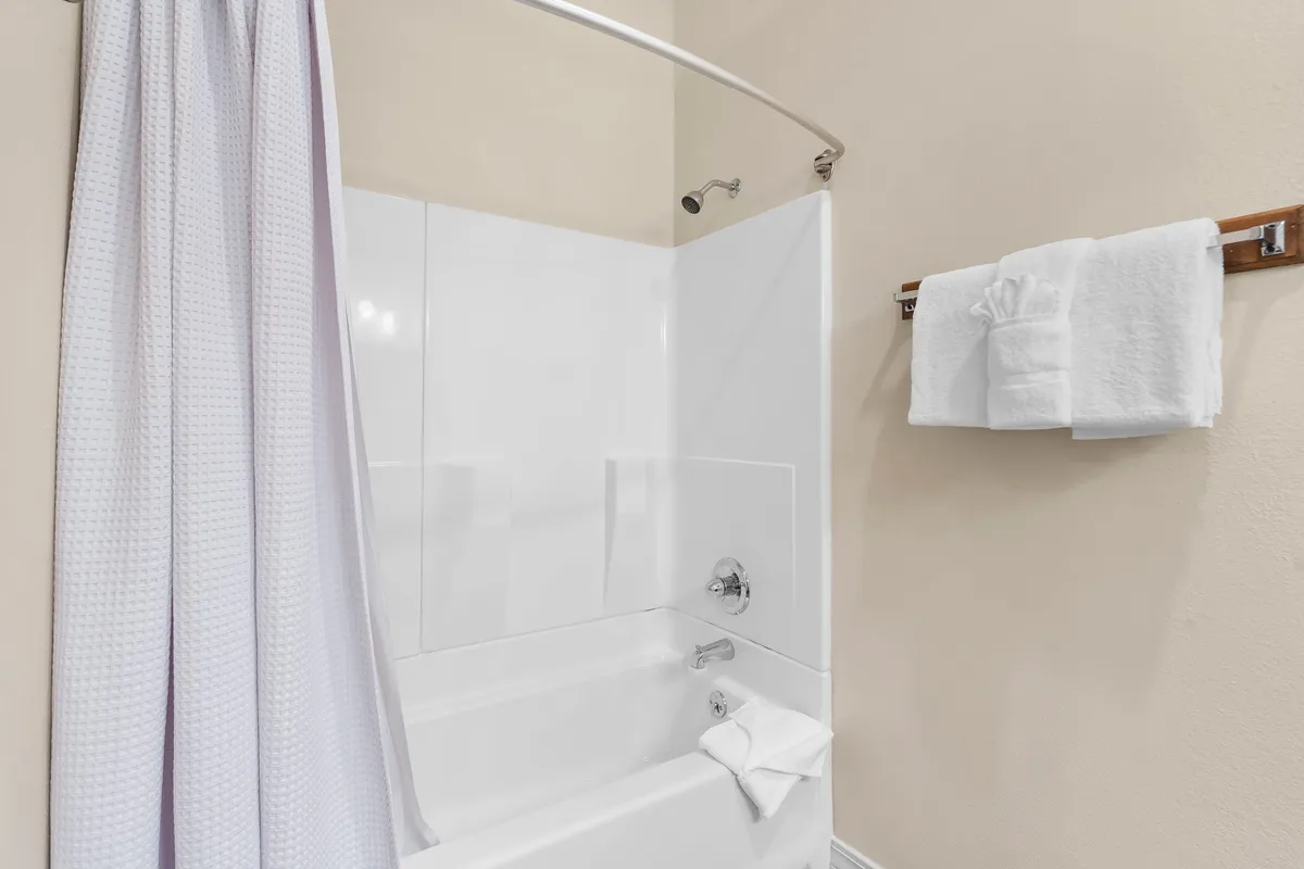 A modern bathroom featuring a bathtub with a shower curtain, fresh towels neatly arranged, and a calming color palette. The space is designed for comfort, privacy, and self-care after a day of adventure.