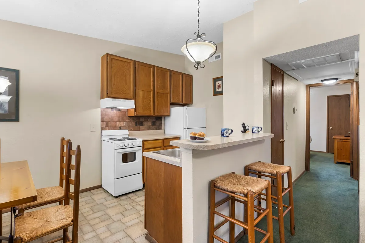 A homey kitchen scene with cabinetry, bar stools, a dining table, and appliances. The arrangement encourages socializing, cooking, and sharing meals, while the decor adds to the vintage and welcoming feel of the interior.