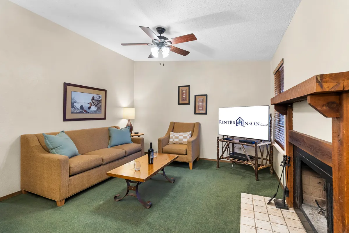 A cozy living room featuring a plush sofa, a glowing fireplace, a coffee table, and a television. The space is arranged for relaxation and group gatherings, with warm lighting and inviting decor that evoke nostalgic evenings by the fire.