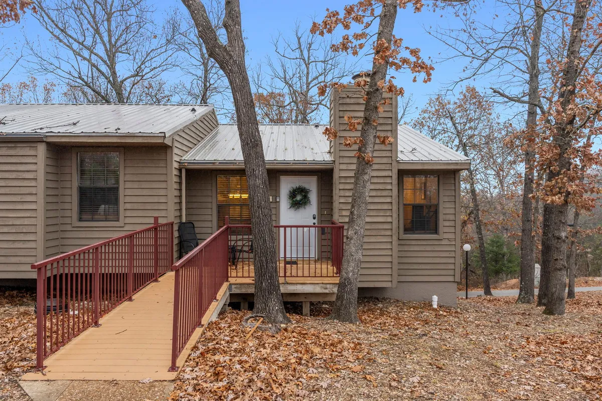 A welcoming front entrance with a wooden ramp, adorned with a wreath on the door, and surrounded by mature trees and autumn leaves. The area offers easy access to outdoor spaces and conveys a sense of warmth and hospitality for both guests and their pets.