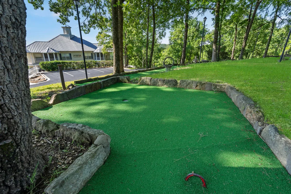 An exterior shot of a mini-golf area nestled among lush green grass and surrounded by mature trees. The scene is lively yet relaxed, with open spaces ideal for friendly competitions and outdoor fun for all ages.