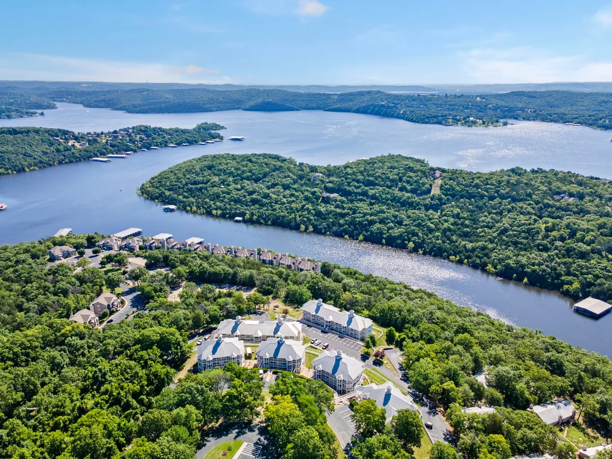 This image captures a tranquil view of Table Rock Lake, with abundant greenery, residential buildings nestled along the shoreline, and a small island in the distance. The calm water reflects the warm glow of sunset, creating a romantic and peaceful atmosphere.